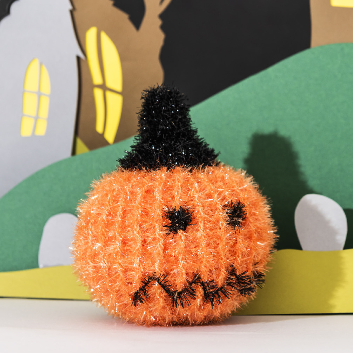 Häkelanleitung Creative Bubble Kürbis: Ein orangefarbener, flauschiger Kürbis mit Gesicht vor einer Halloween-Kulisse.