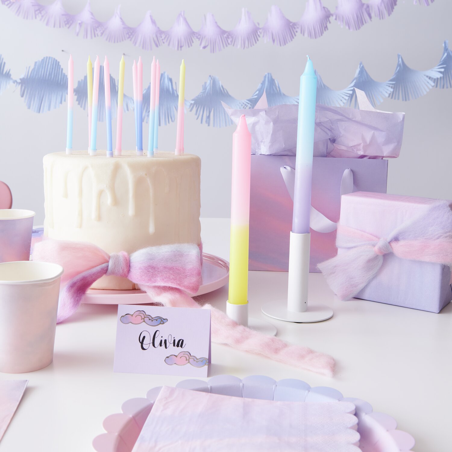 Kerze Dip Dye: Bunte Kerzen in Blau, Pink und Gelb dekorieren einen Geburtstagstisch mit pastellfarbenen Geschenken und Torte.
