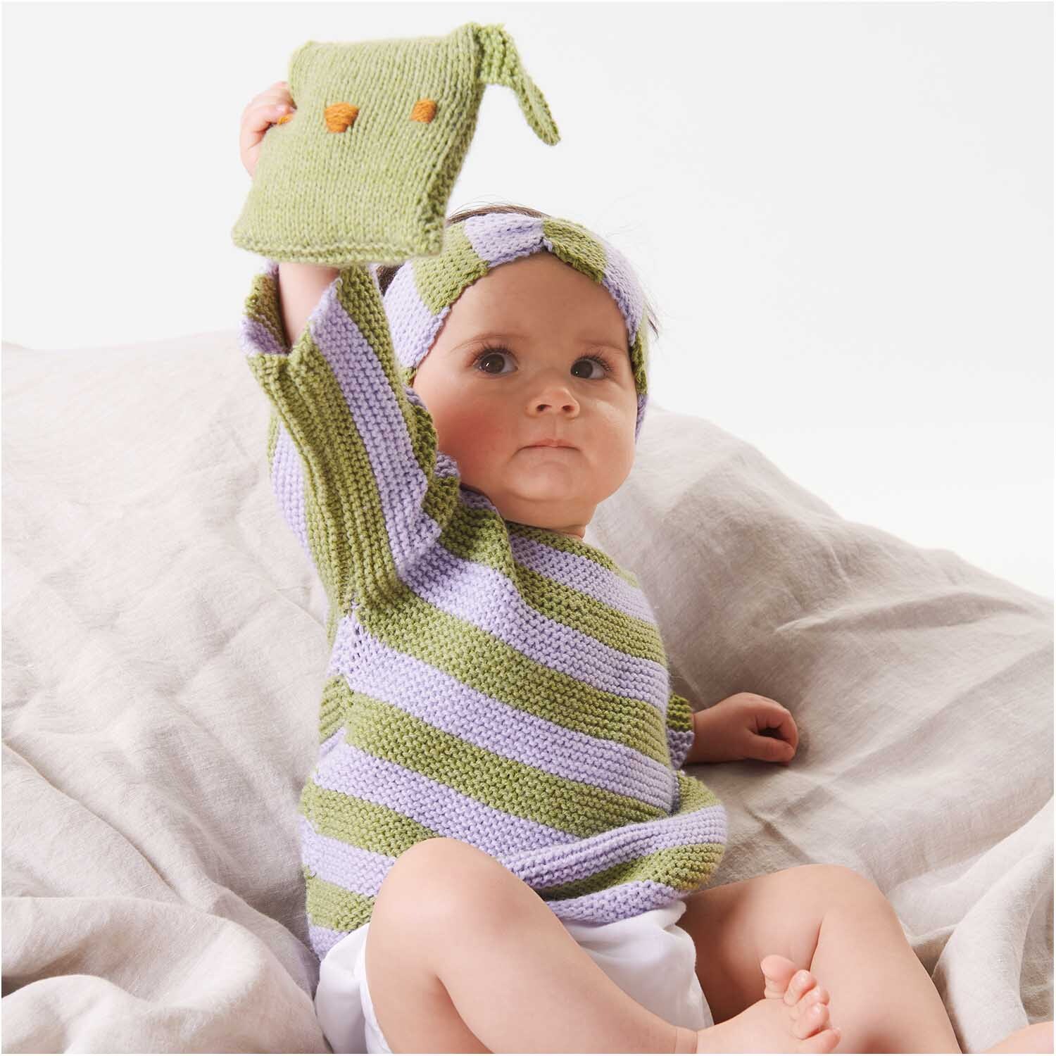 Rico Baby Classic dk: Baby in gestreiftem Strickoutfit in Pistazie und Lila, hält gestricktes Accessoire.