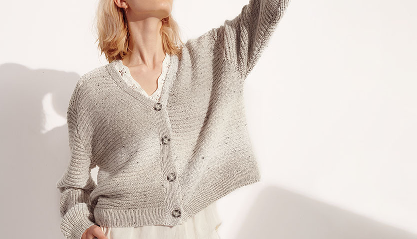 Strickanleitung Jacke aus Fashion Cotton Light & Long Tweed dk: Frau trägt graue Strickjacke mit Knöpfen, stilvoll und modern in Szene gesetzt.