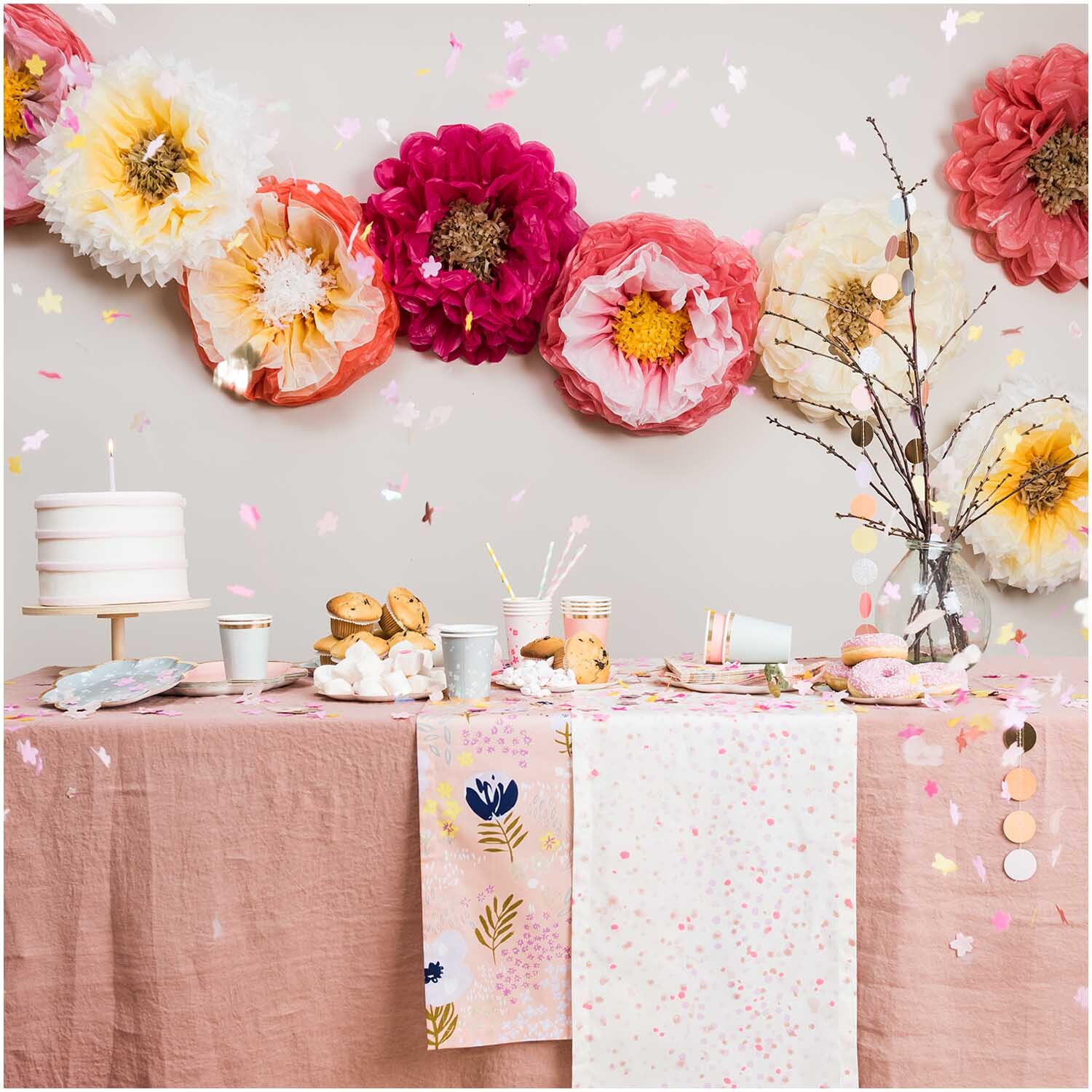 Pappbecher Blüten rosa 200ml 12 Stück, dekoriert auf einem Tisch mit rosa Tischdecke und großen Papierblumen im Hintergrund.