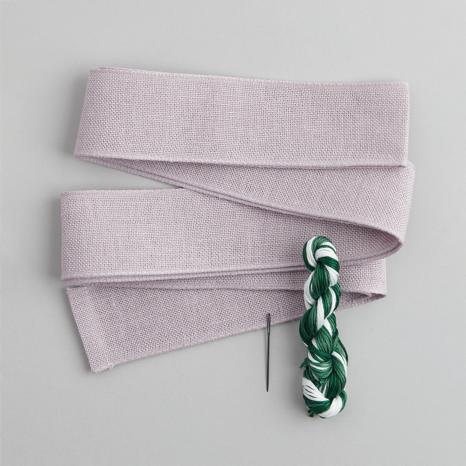 Stickpackung Schleife Maiglöckchenranke von Rico Design zeigt ein lila Band mit grün-weißer Stickgarnrolle und Nadel. Ideal für kreative Projekte.