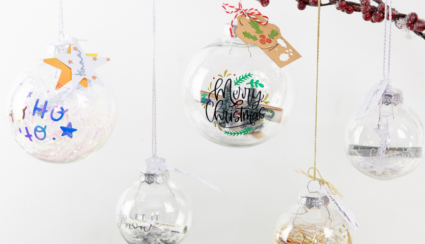 Bastelanleitung Weihnachtskugeln beplotten: Fünf dekorierte Kugeln mit festlichen Motiven und Anhängern.