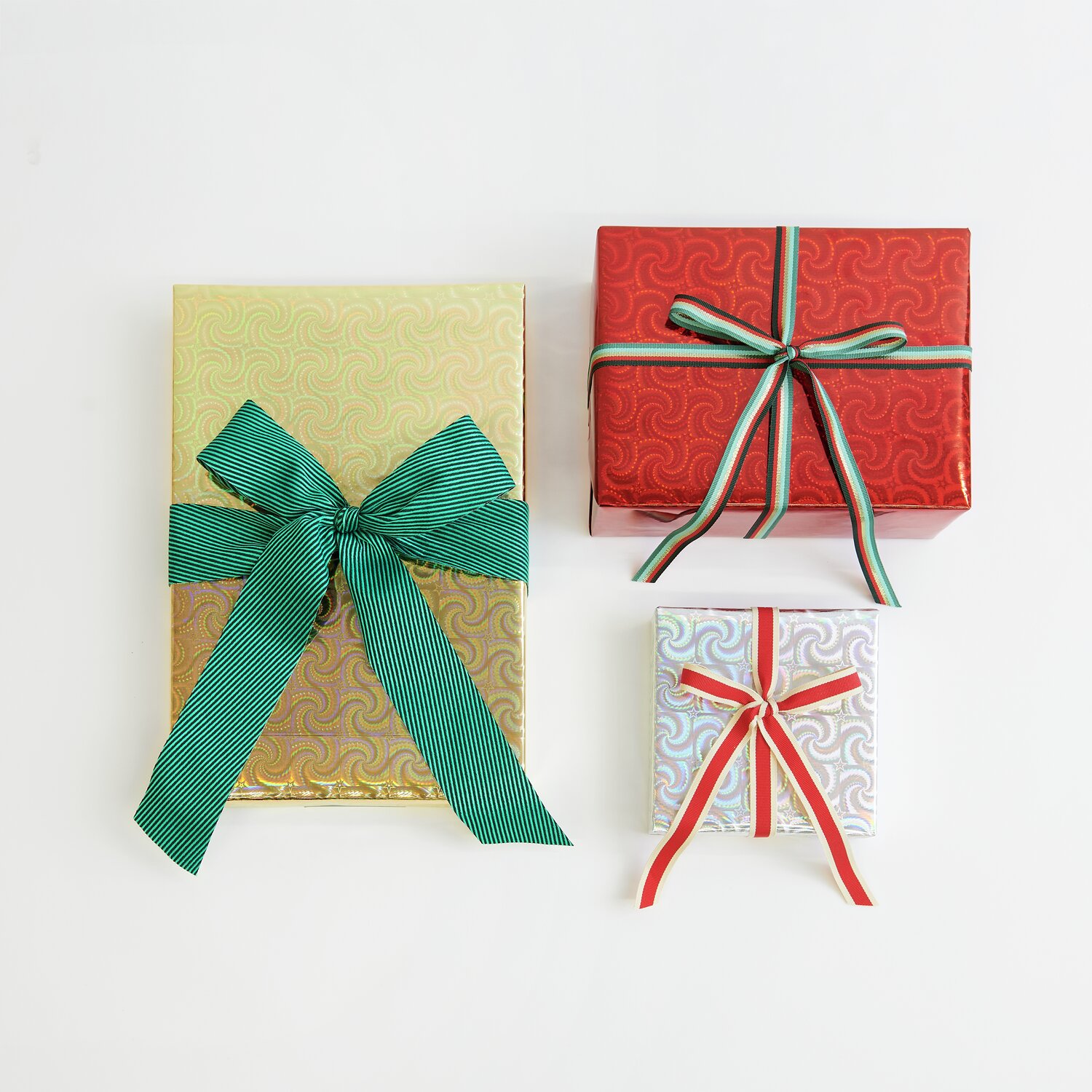 Paper Poetry Geschenkpapier Holographisch mit Sternen Mix: Drei Geschenke in Gold, Rot und Silber, verziert mit grünen und roten Bändern.