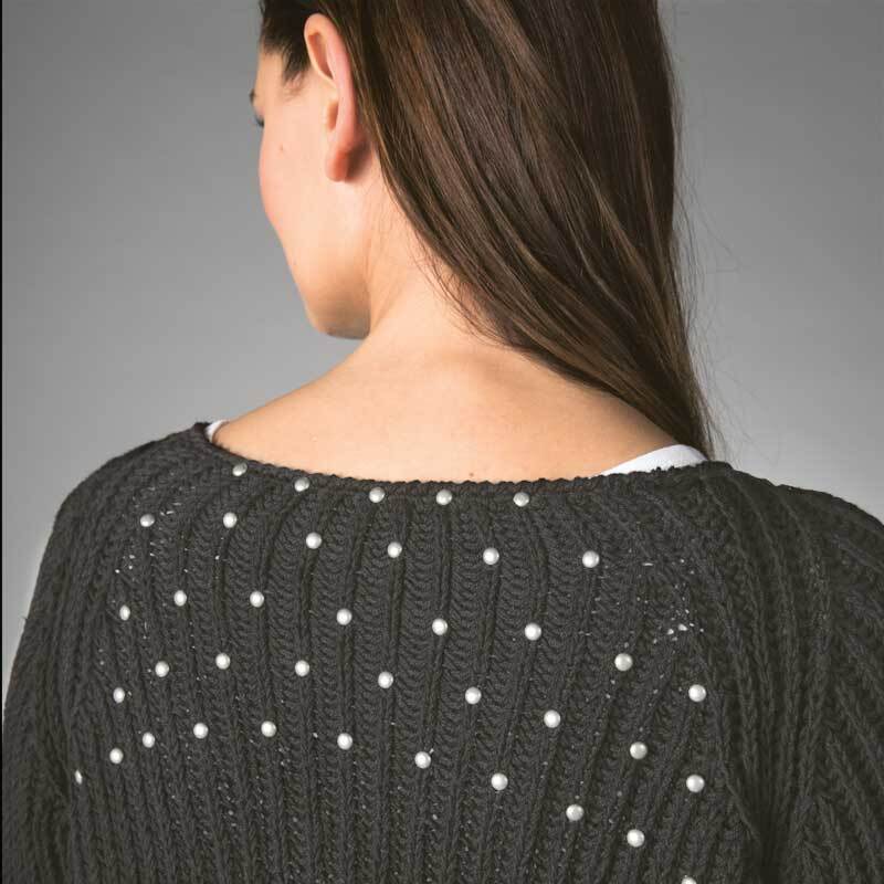 Sport- & Strumpfwolle Cotton Stretch: Frau trägt einen gestrickten Pullover mit Perlenmuster auf dunklem Stoff. Ideal für stilvolle Strickprojekte.