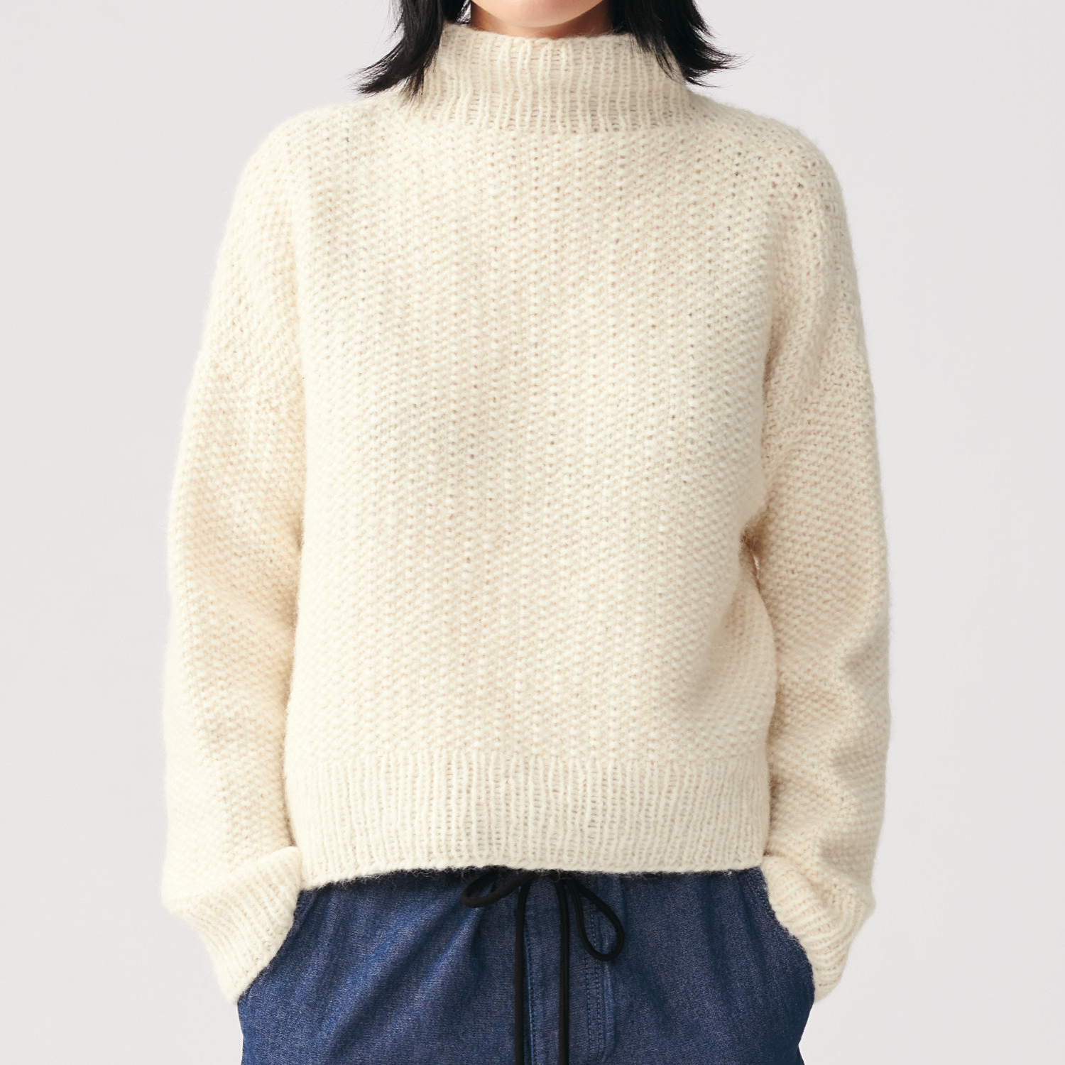 Strickanleitung Damenpullover aus Luxury Baby Alpaca & Merino chunky. Der Pullover ist cremefarben und hat einen hohen Kragen, getragen von einer Frau.