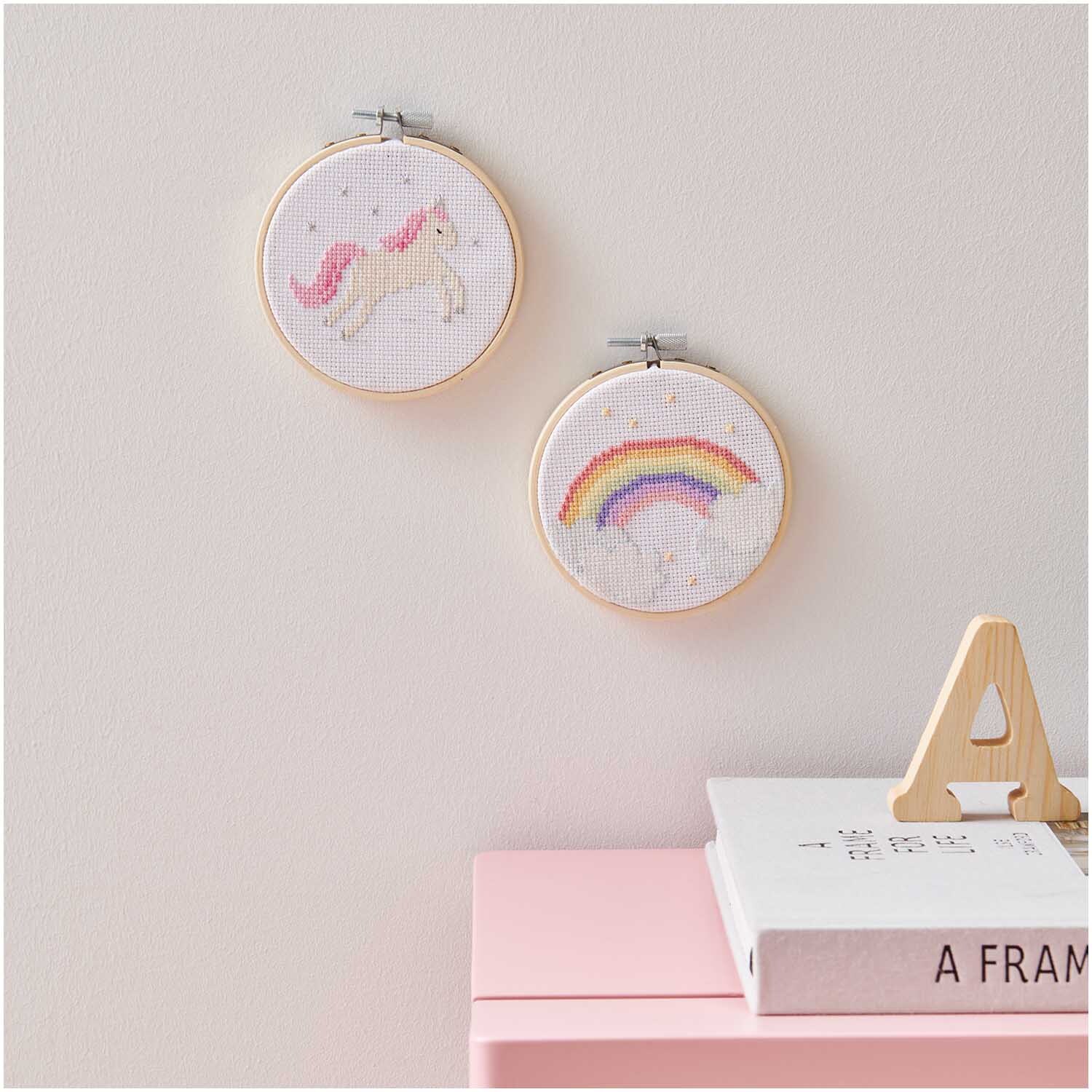 Stickpackung Mini Kit Einhorn Bild Ø 10cm zeigt ein Einhorn und einen Regenbogen in Stickrahmen an der Wand.