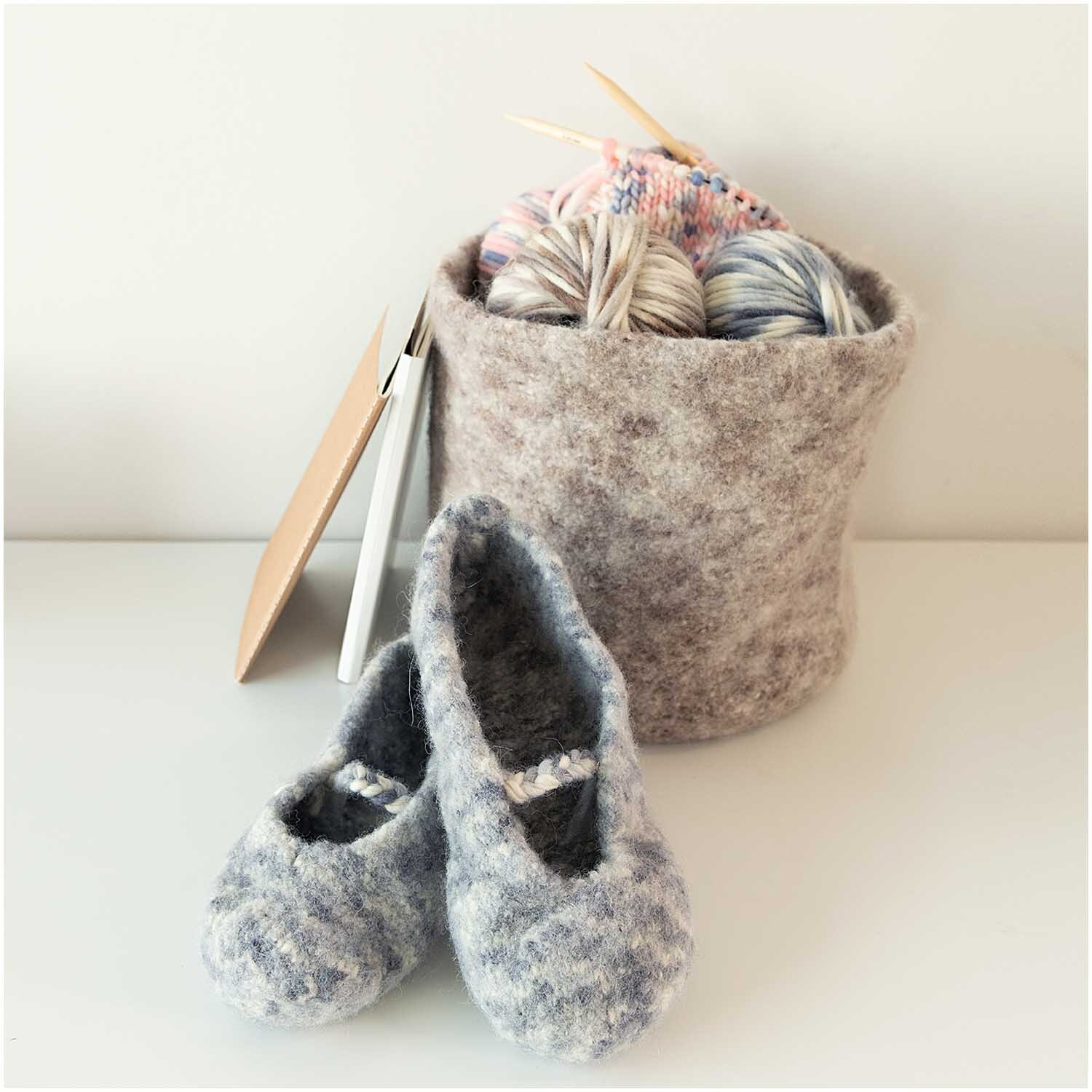 Creative Filz Print: Graue Filzpantoffeln und ein Korb mit Strickgarn von Rico Design auf weißem Hintergrund.