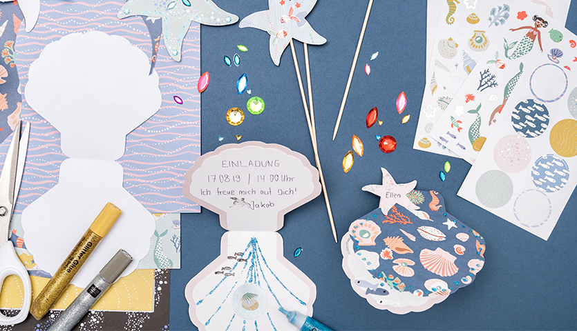 Bastelanleitung Mermaid-Einladungen & -deko: Kreatives Set mit Muschelmotiven, Stickern und Bastelmaterialien auf blauem Hintergrund.