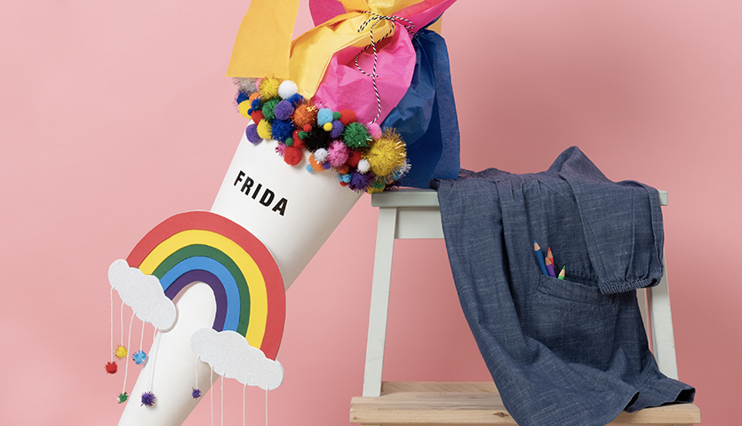 Bastelanleitung Regenbogenschultüte: Bunte Schultüte mit Pompons und Regenbogenmotiv auf rosa Hintergrund.