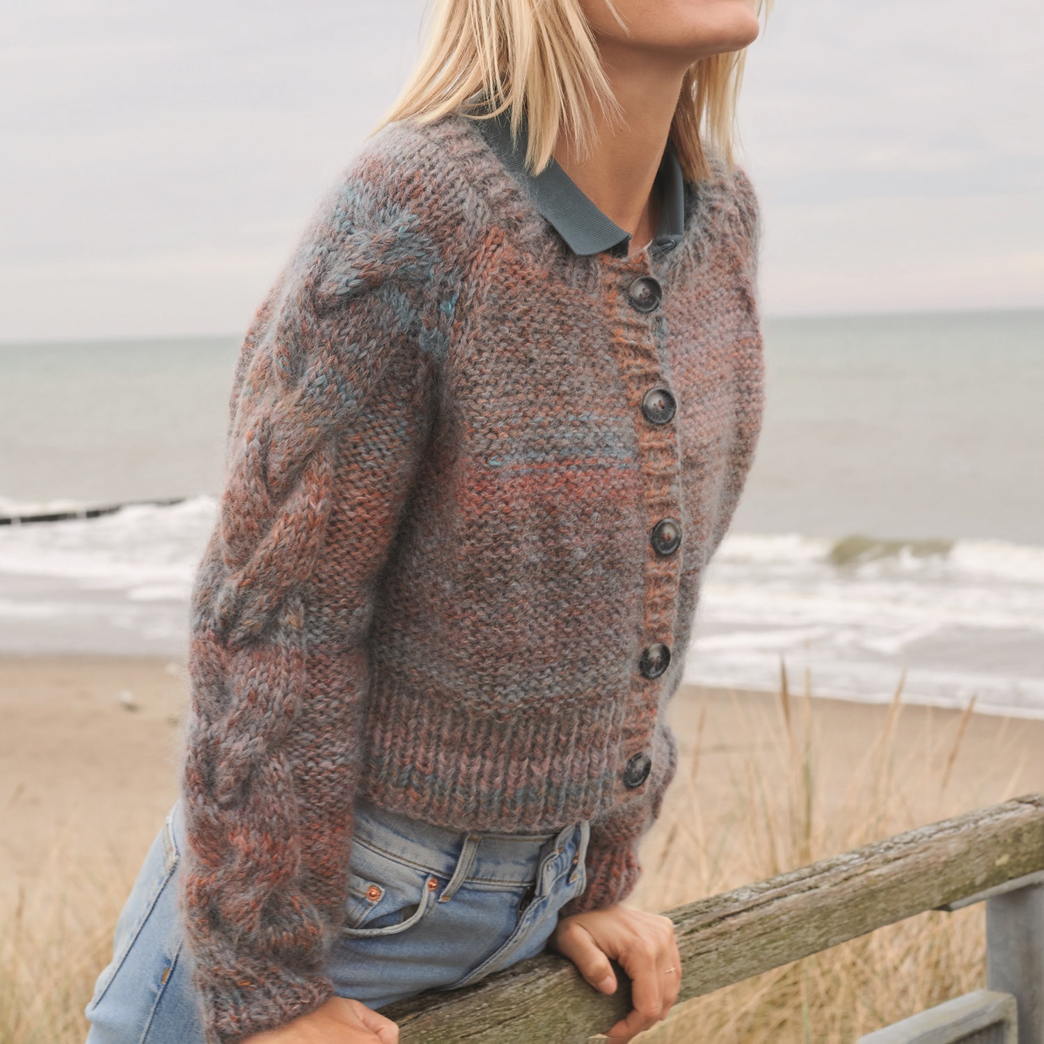 Strickanleitung Jacke aus Creative Mohair Melange: Frau lehnt an einem Geländer, trägt gestrickte Jacke mit Knöpfen.