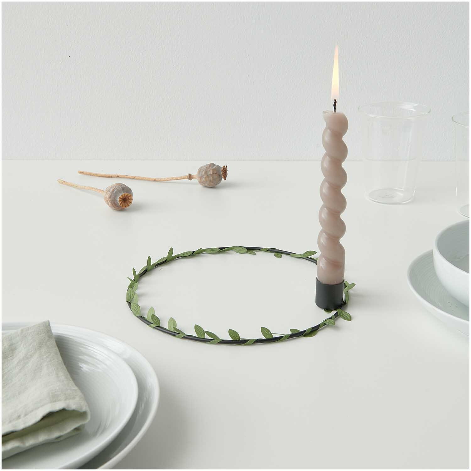 Metallring mit Kerzenhalter Ø 20cm von Rico Design in Schwarz Matt, dekoriert mit grünen Blättern und einer brennenden Kerze auf einem Tisch.