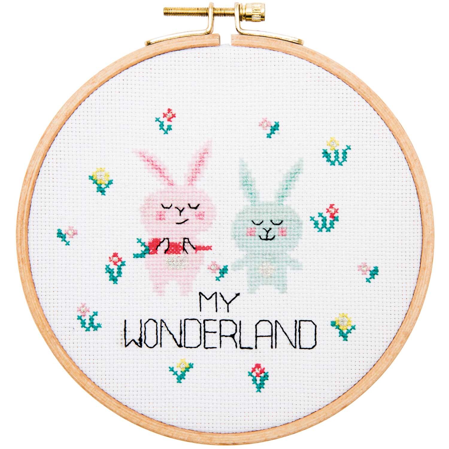 Stickpackung Hasenpaar Wonderland 15,5cm zeigt zwei gestickte Hasen in einem Holzrahmen, umgeben von bunten Blumen.