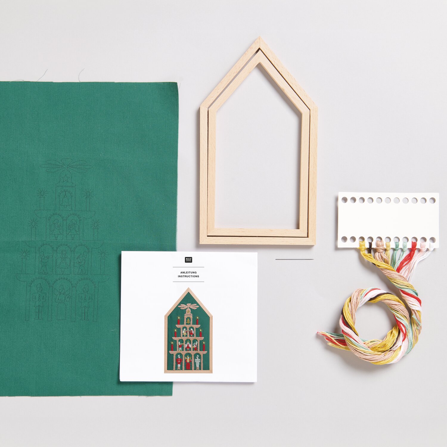 Stickpackung Pyramide vorgezeichnet: Grüner Stoff, Holzrahmen, Garn und Anleitung von Rico Design. Ideal für kreative Handarbeiten.