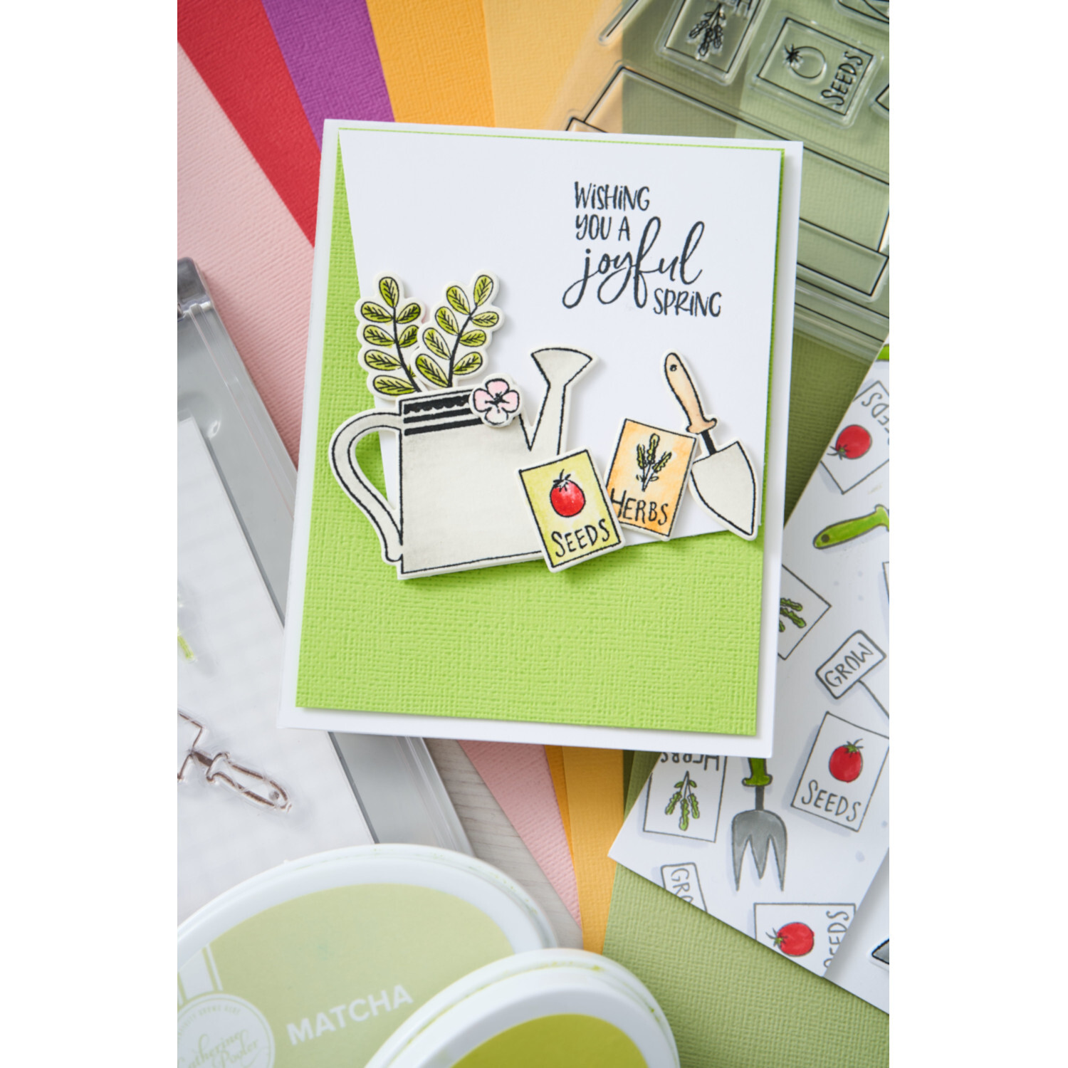 Thinlits Die Set Greenhouse Finds #2 18PK zeigt eine frühlingshafte Karte mit Gießkanne, Samen und Gartenwerkzeug auf grünem Hintergrund.