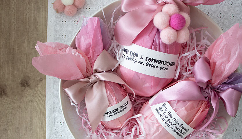 Inspiration Geschenkverpackung für Ostern: Rosa Verpackungen mit Schleifen und Filzblumen auf einem Teller.