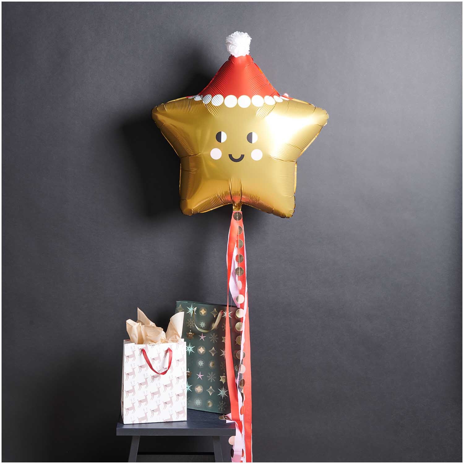 Folienballon Weihnachten Stern in Gold mit Weihnachtsmütze, dekoriert neben Geschenktüten.