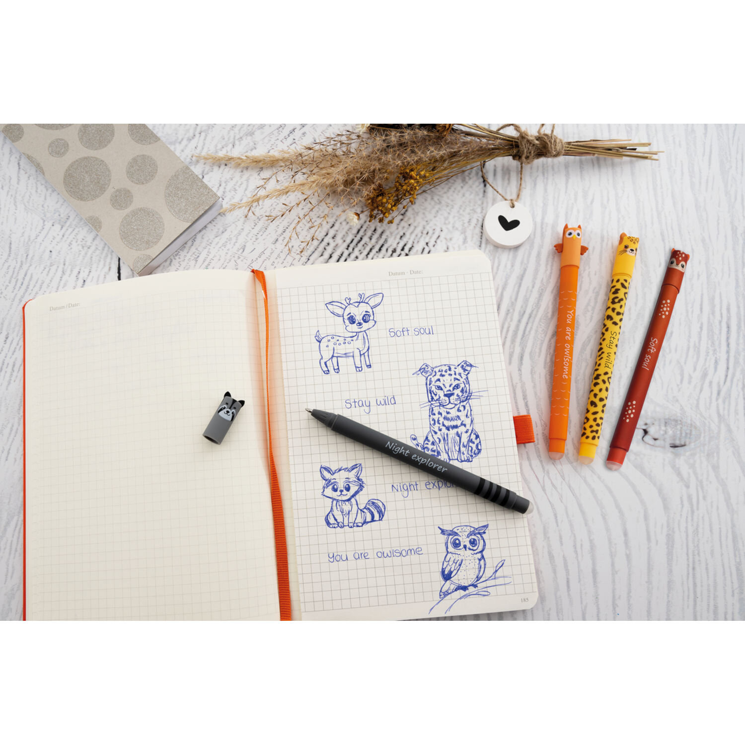 Gelschreiber Animal Erase it von Eberhard Faber neben offenem Notizbuch mit Tierzeichnungen, drei radierbaren Stiften im Tierdesign und schwarzem Stift auf hellem Holztisch